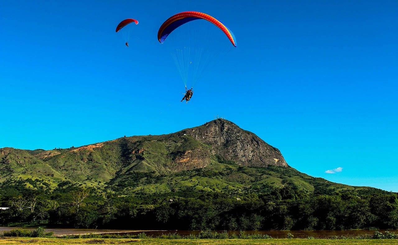 Parapentes no céu azul diante do Pico da Ibituruna